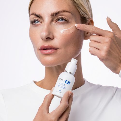 Frau hält eine weiße Flasche mit Zerstäuber. Sie berührt ihre Haut mit dem Finger, auf dem sich eine Creme befindet. Aufschrift IMAGE MD.