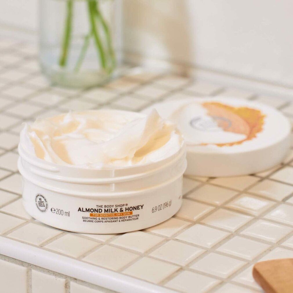 Offene Dose Body Butter, daneben der Deckel. Aufschrift: Almond Milk & Honey. 200 ml.