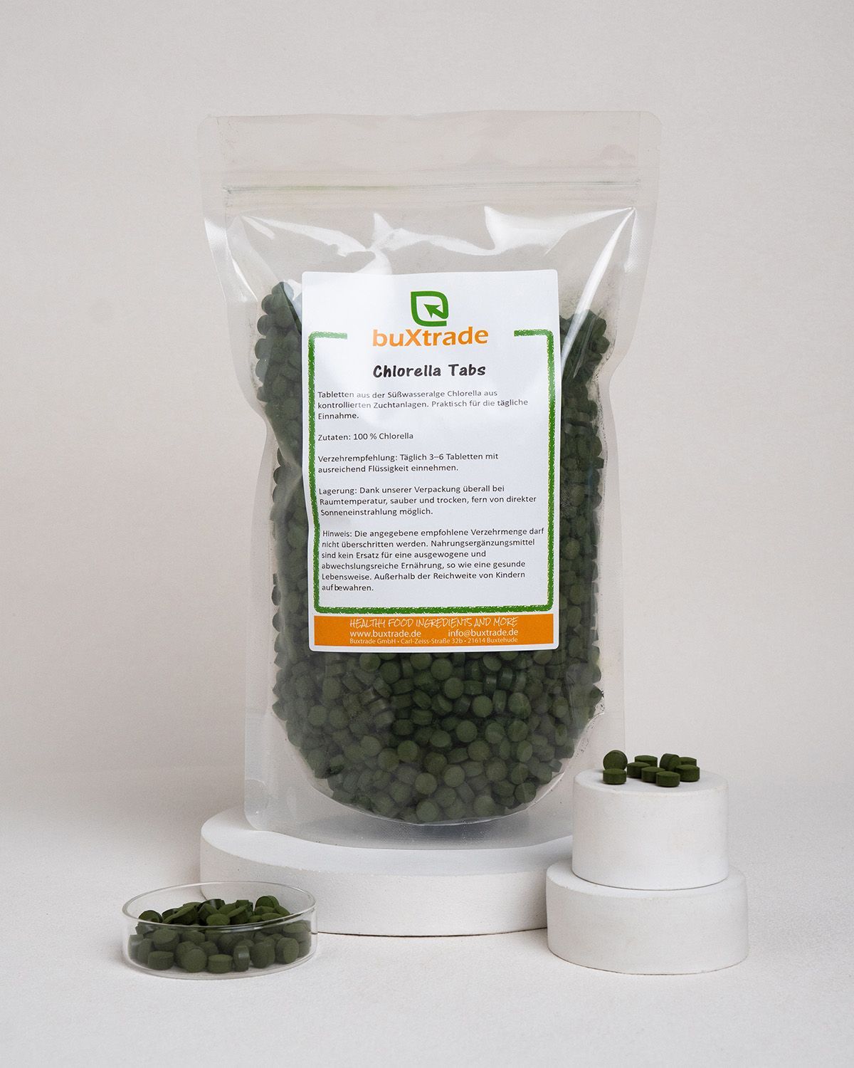 Beutel mit Chlorella Tabs, daneben Schale mit Tabs und Podest mit Tabs. Transparente Verpackung.