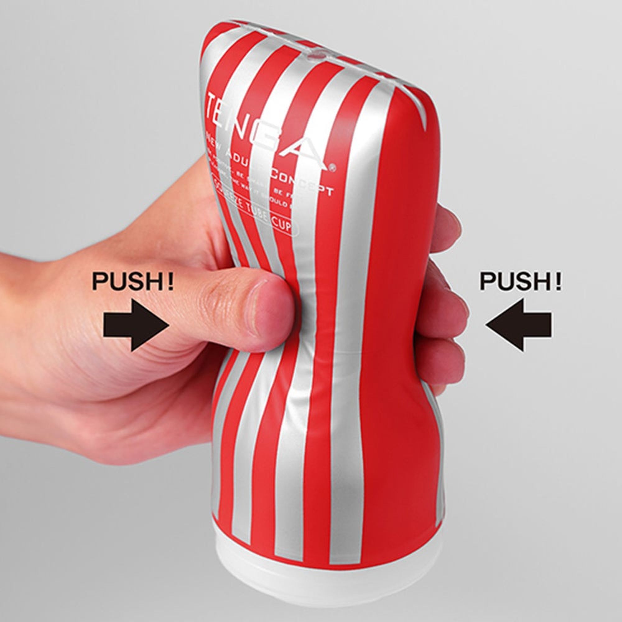 Hand drückt TENGA Soft Tube Cup zusammen. Roter Körper mit weißen Streifen. Pfeile zeigen Druckrichtung.