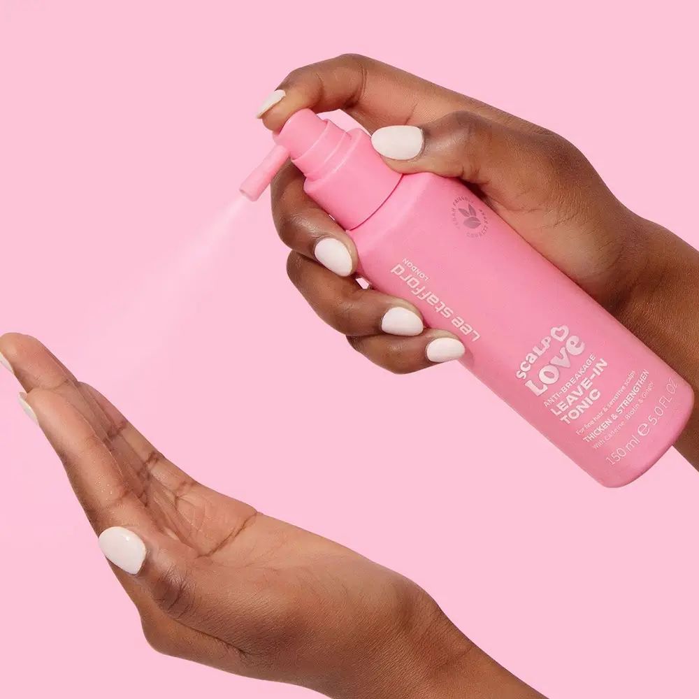 Hände halten rosa Flasche mit Sprühkopf. Sprühnebel sichtbar. Aufschrift: Scalp Love Leave-in Tonic. Marke: Lee Stafford. Vegan-Logo.