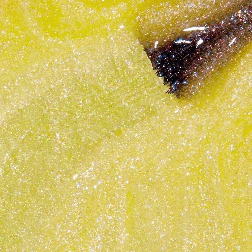 Nagellack-Applikator mit gelbem Lack auf gelbem Hintergrund. Der Pinsel ist mit Glitzerpartikeln bedeckt.