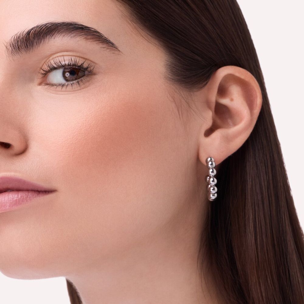 Nahaufnahme einer Frau. Sie trägt Ohrringe. Rouge ist auf den Wangen zu sehen.