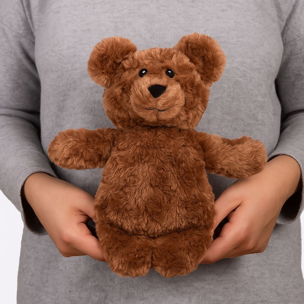 Brauner Teddybär, gehalten von Händen. Weiches Material, Ohren, Augen, Nase und Mund erkennbar. Helle Umgebung.