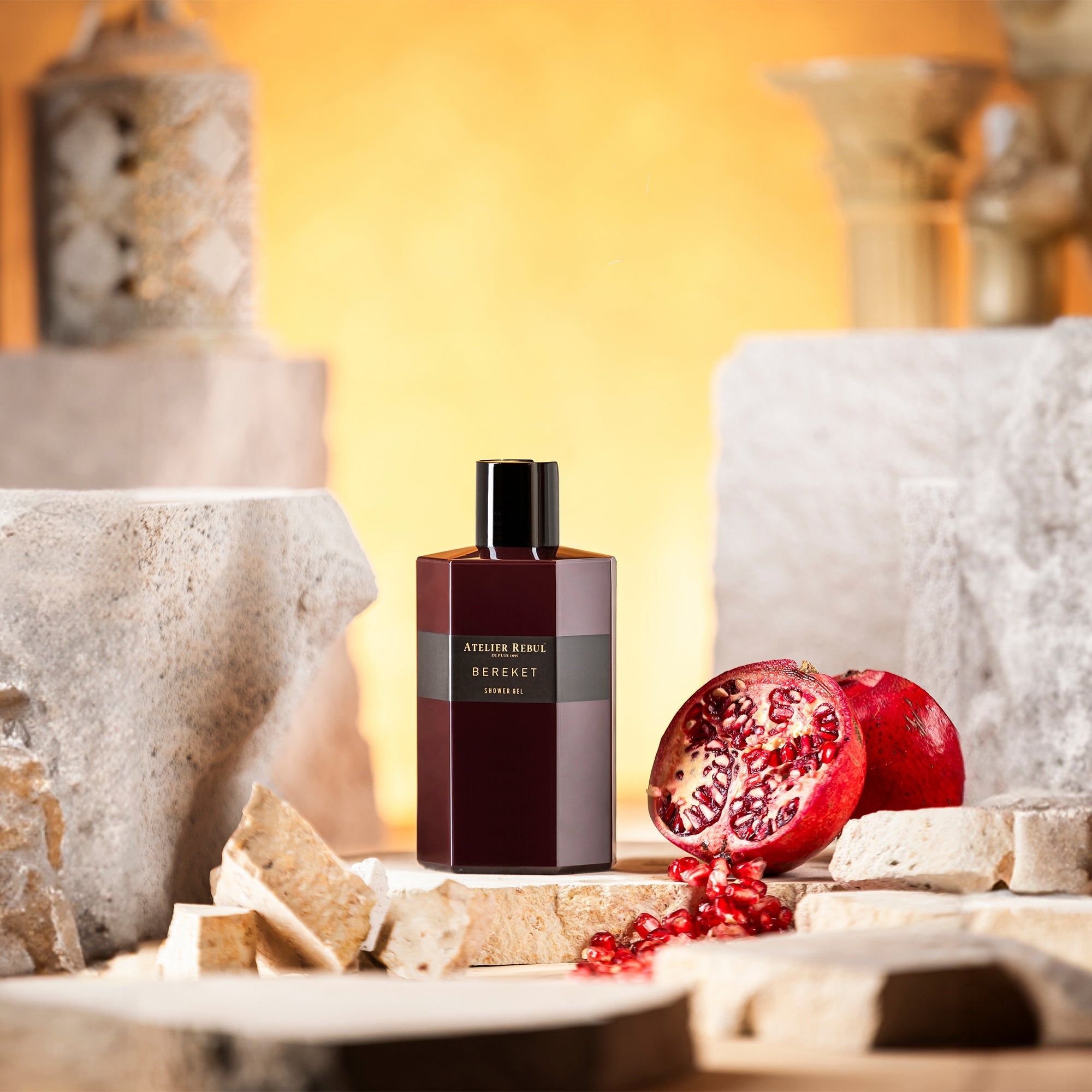 Bordeauxfarbenes Duschgel mit Granatapfel. Aufschrift: Atelier Rebul Bereket. Flasche mit schwarzem Deckel, auf Steinen platziert.