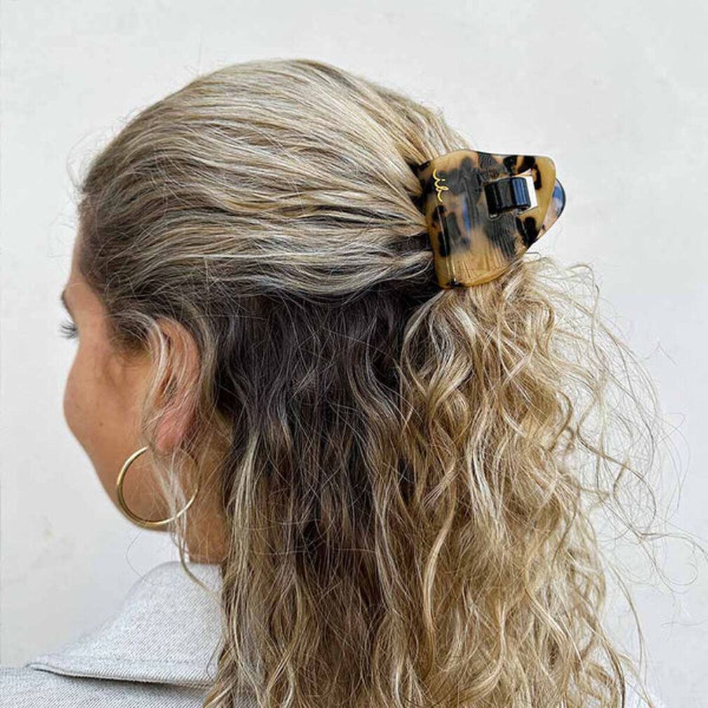 Frau mit blonden Locken, die eine Haarspange mit Leopardenmuster trägt. Goldener Ohrring.
