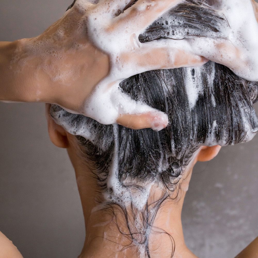 Hände waschen Haare mit Schaum. Rückansicht einer Person.