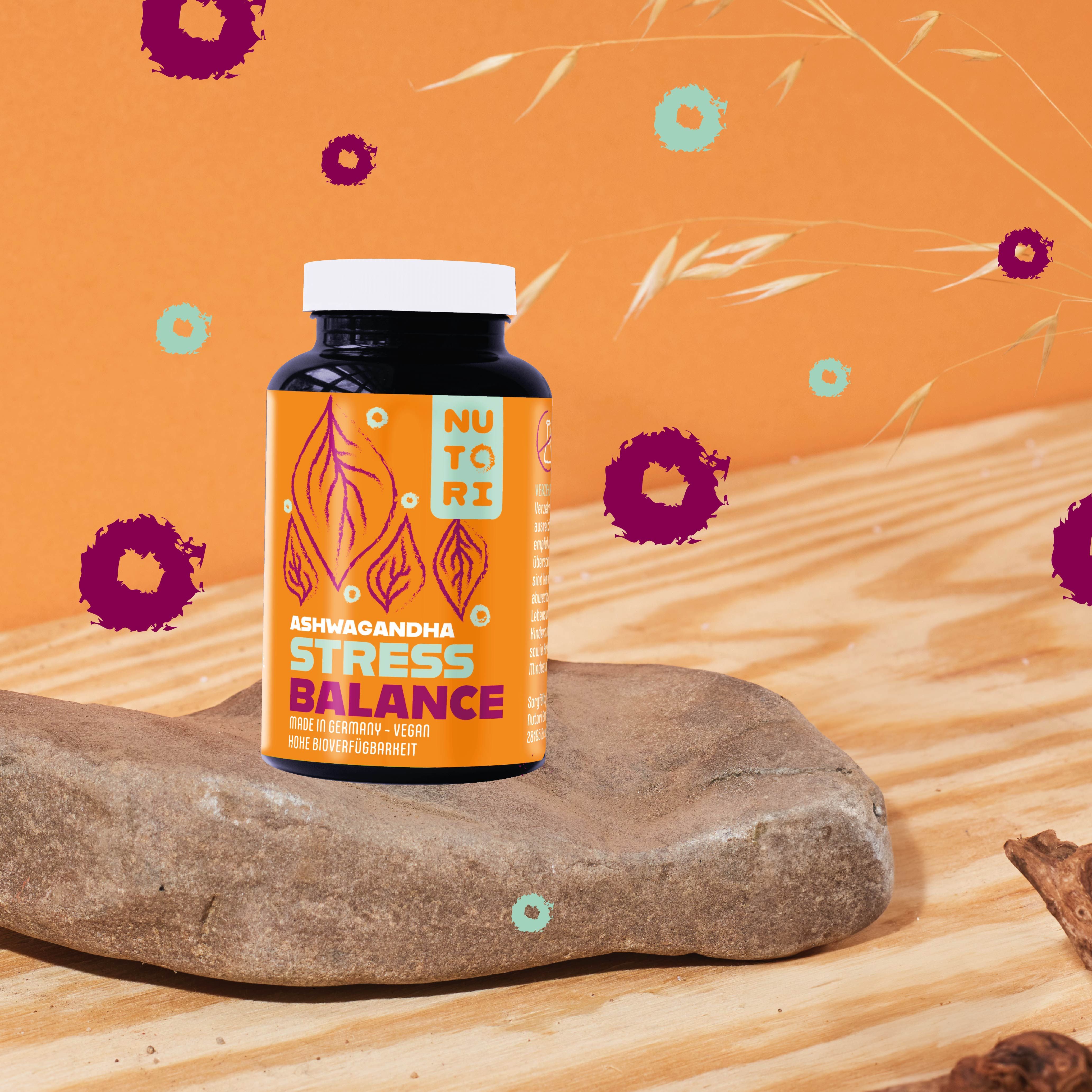 Braune Flasche mit weißem Deckel auf einem Stein. Aufschrift: Nutori Ashwagandha Stress Balance. Hintergrund: orangefarben und grün.