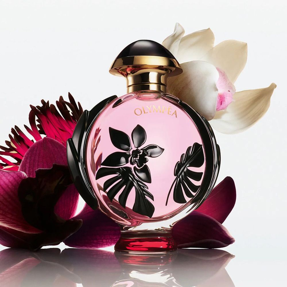 Runder Flakon mit rosa Flüssigkeit, schwarzem Blumendekor und goldfarbenem Verschluss. Blütenblätter umgeben den Flakon.