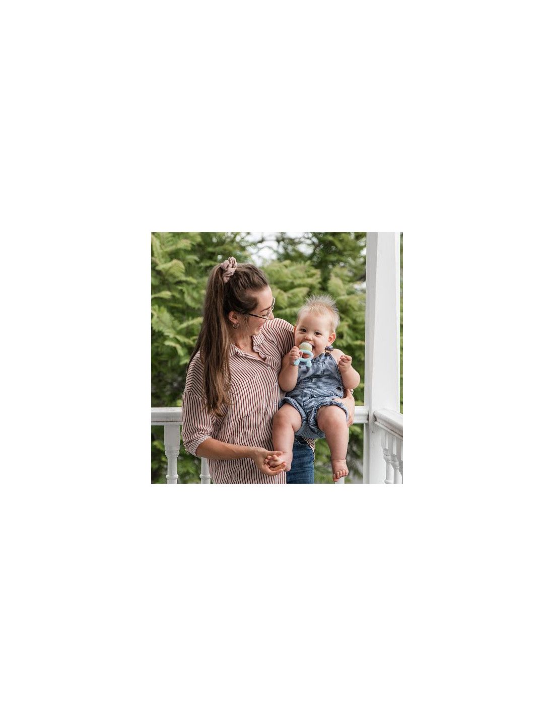 Eine Frau hält ein Baby, das einen blauen Haakaa Fruchtsauger und Beissring (2 in 1) im Mund hat.
