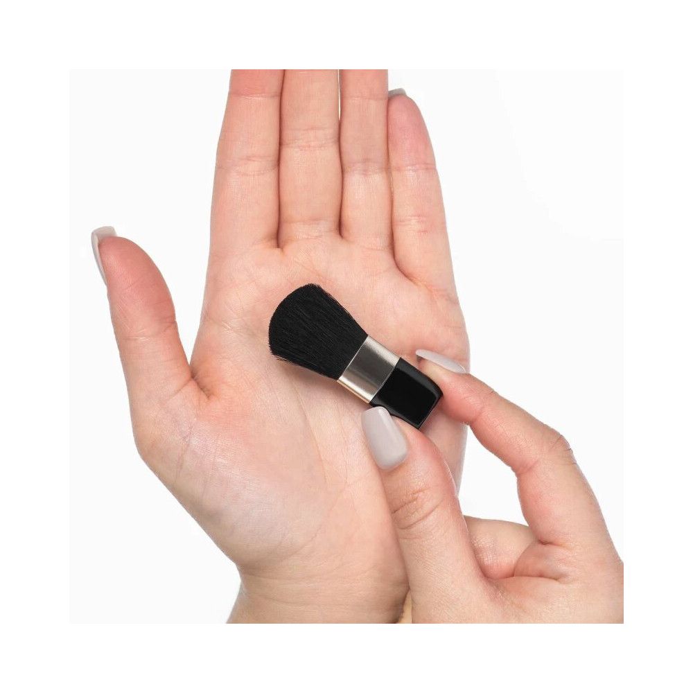 Schwarzer Rougepinsel in Hand gehalten. Schwarze Borsten, silberne Manschette, schwarzer Griff. Gehalten von einer Hand.