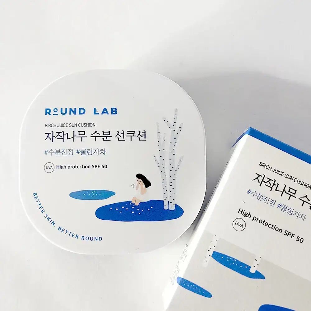 Weiße, quadratische Verpackung mit Produkt und Text: ROUND LAB, Birch Juice Sun Cushion. Illustration. Daneben eine Schachtel.
