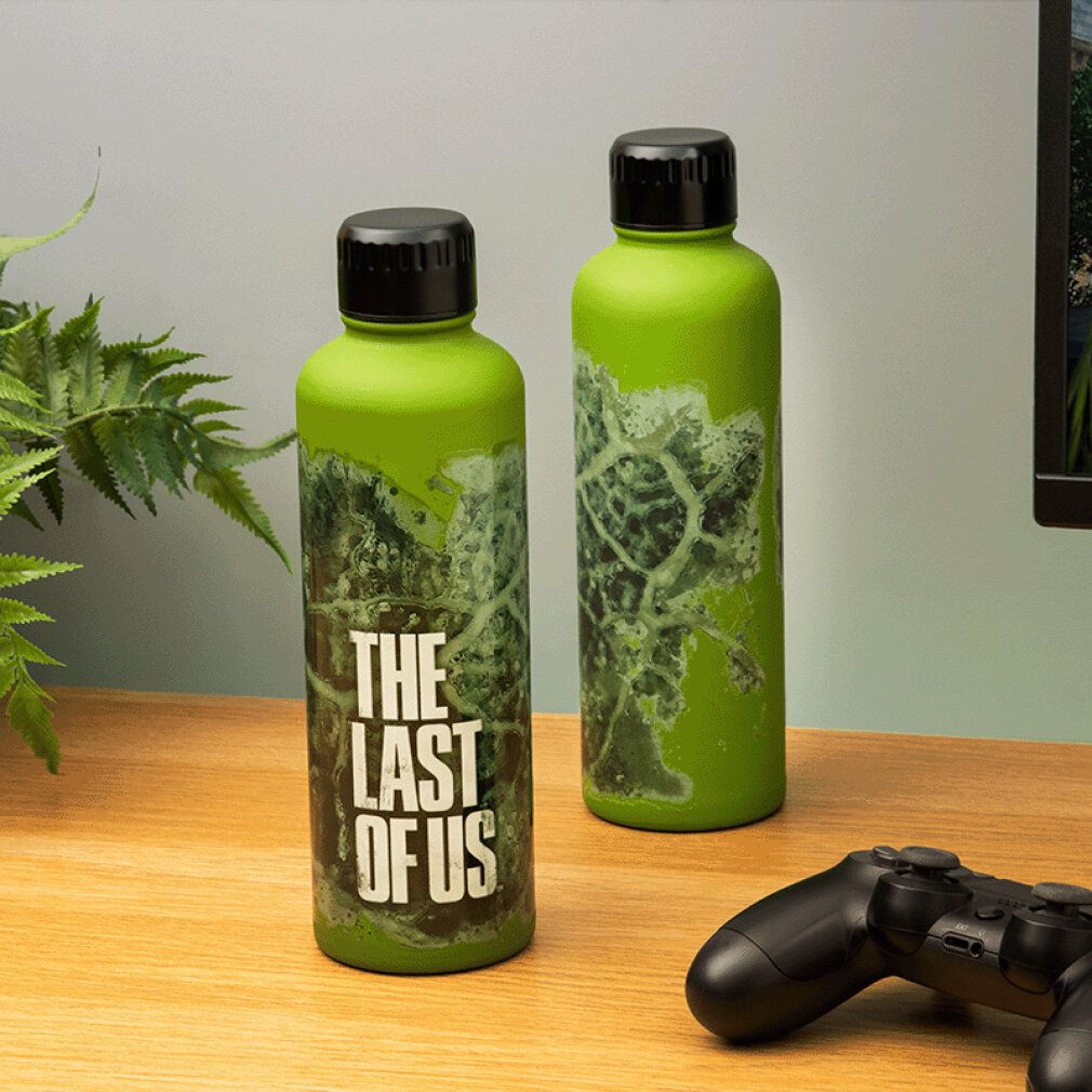 Zwei grüne Metallflaschen mit schwarzen Deckeln. Aufdruck: "THE LAST OF US". Auf Tisch. Controller.
