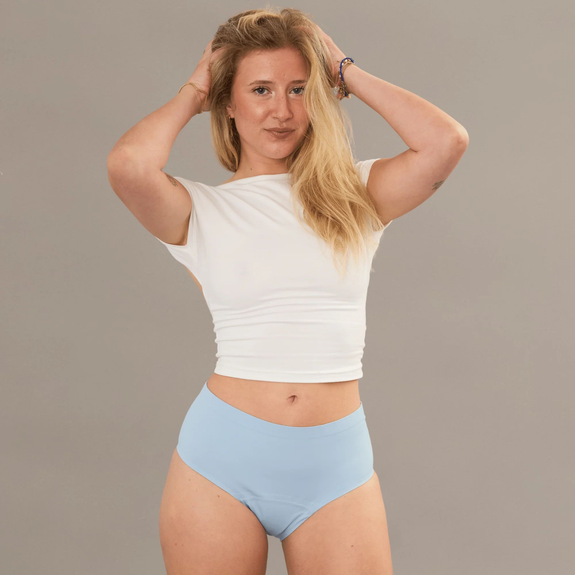 Hellblaue, auslaufsichere Unterhose. Frau mit blonden Haaren und weißem Top. Hände in den Haaren.