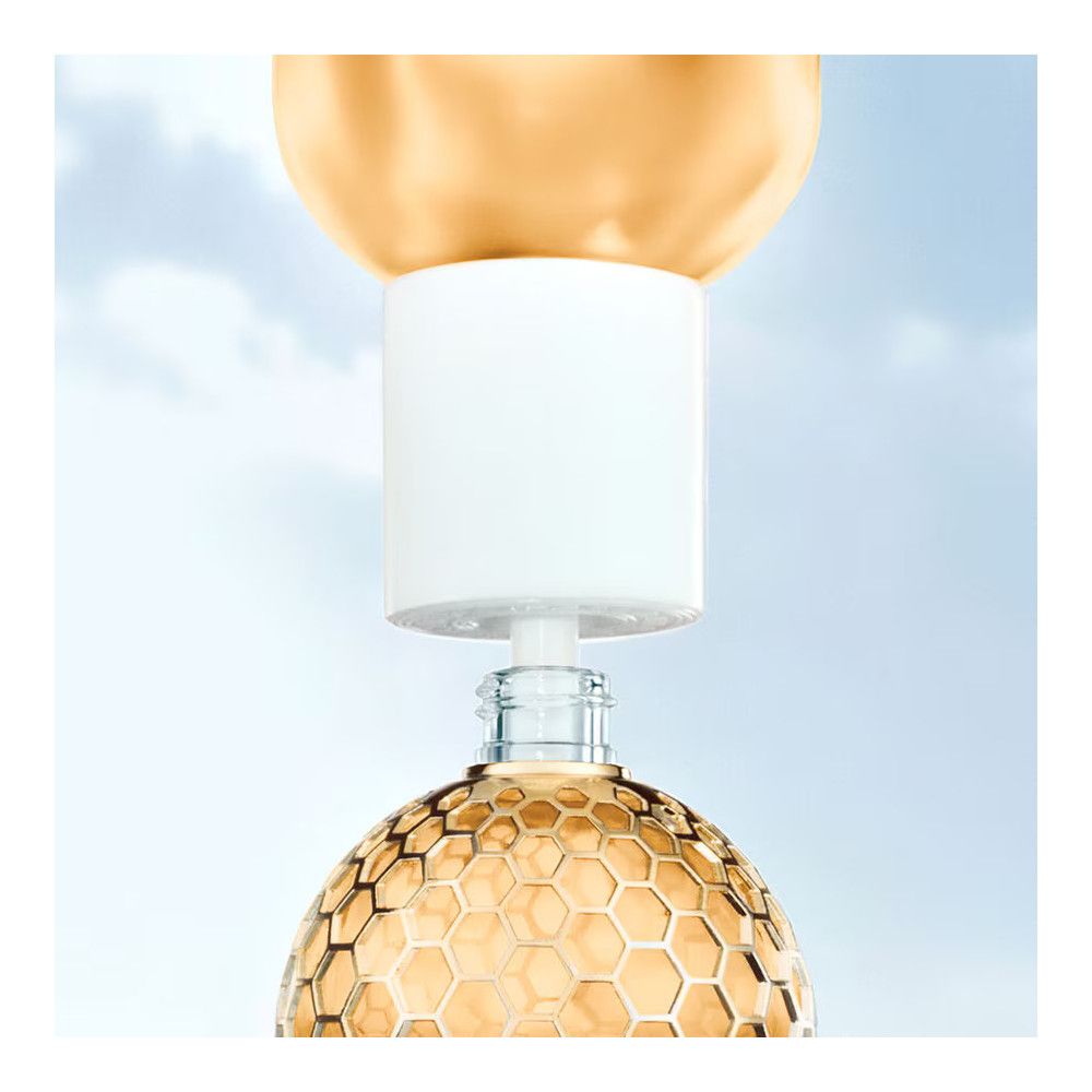 Parfümflasche mit goldfarbenem Wabenmuster-Dekor und weißem Aufsatz. Detailaufnahme, blauer Hintergrund.