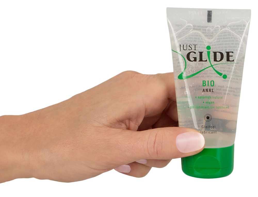 Hand hält eine Tube mit grünem Verschluss. Aufschrift: JUST GLIDE BIO ANAL. Produkt in transparenter Verpackung.
