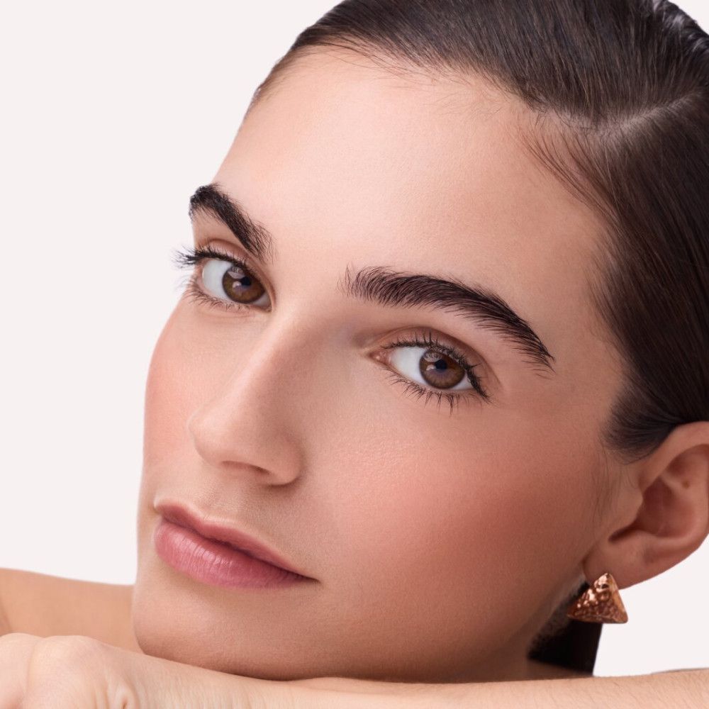 Nahaufnahme einer Frau mit gebräunter Haut. Sie trägt goldene Ohrringe. Auf ihren Wangen ist Rouge aufgetragen.