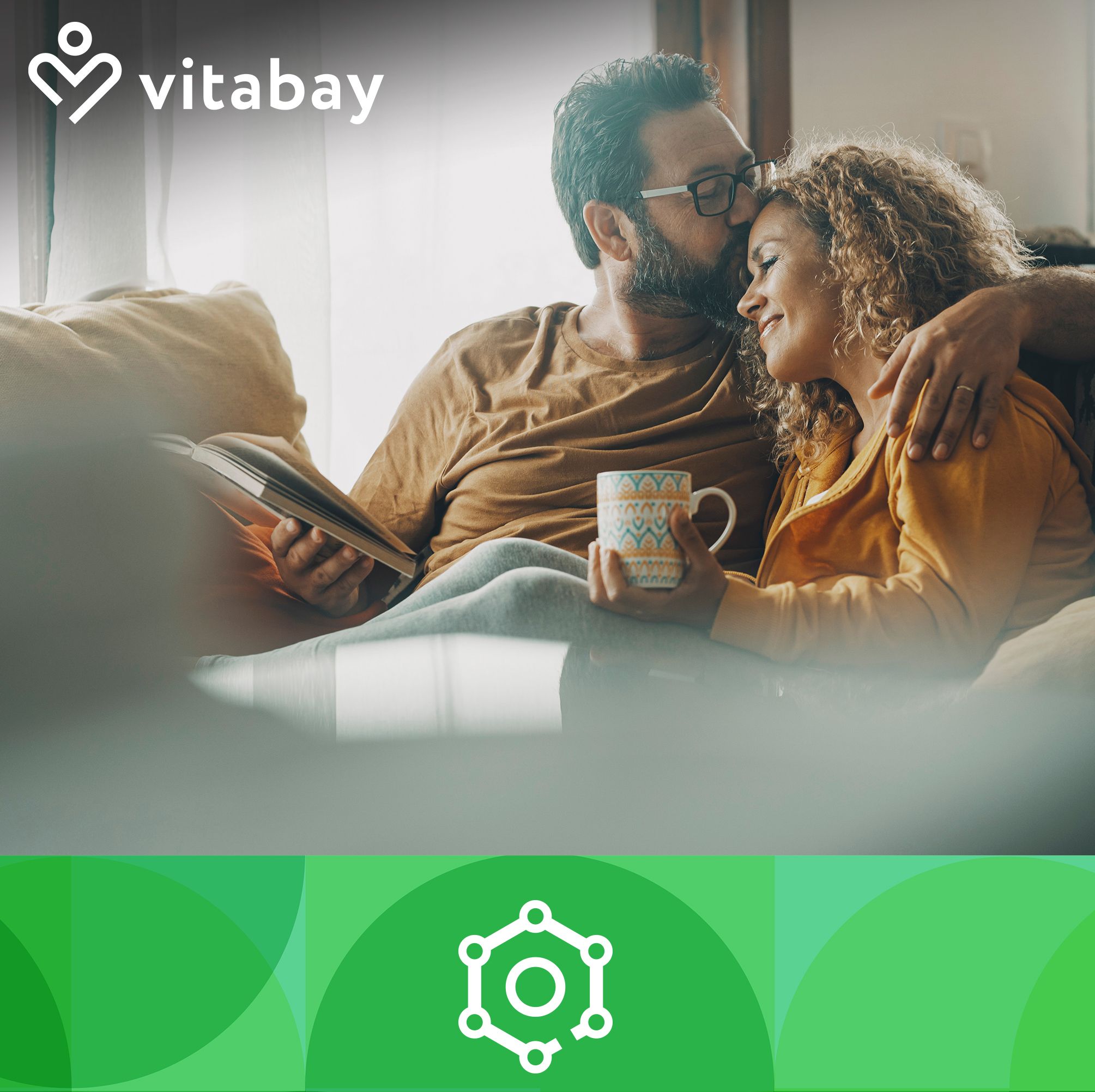 Ein Mann und eine Frau umarmen sich. Im Hintergrund ein Sofa und eine Tasse. Logo: Vitabay.