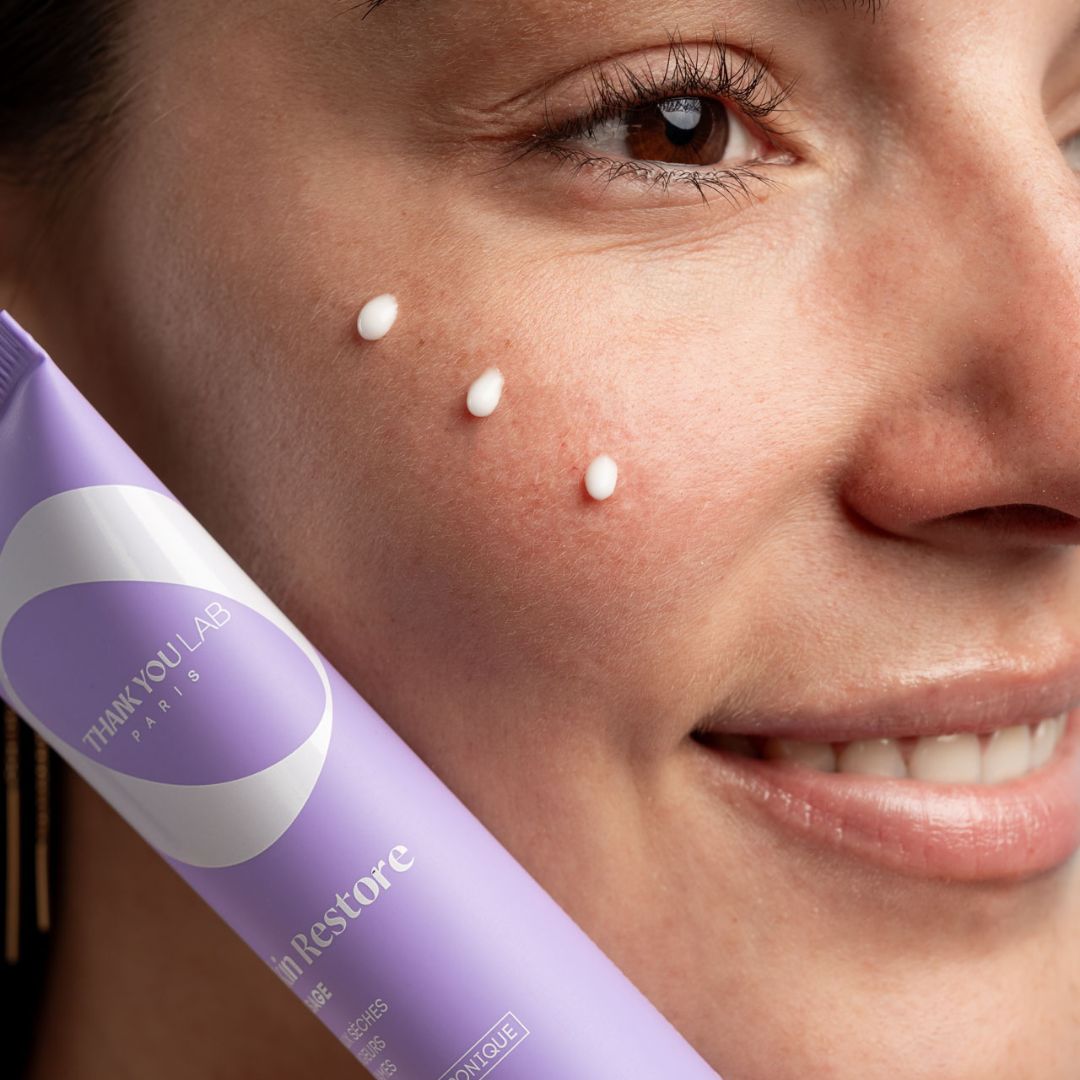 Lila Tube mit weißer Creme. Auf der Haut sind drei Cremepunkte zu sehen. Aufschrift: THANK YOU LAB PARIS.