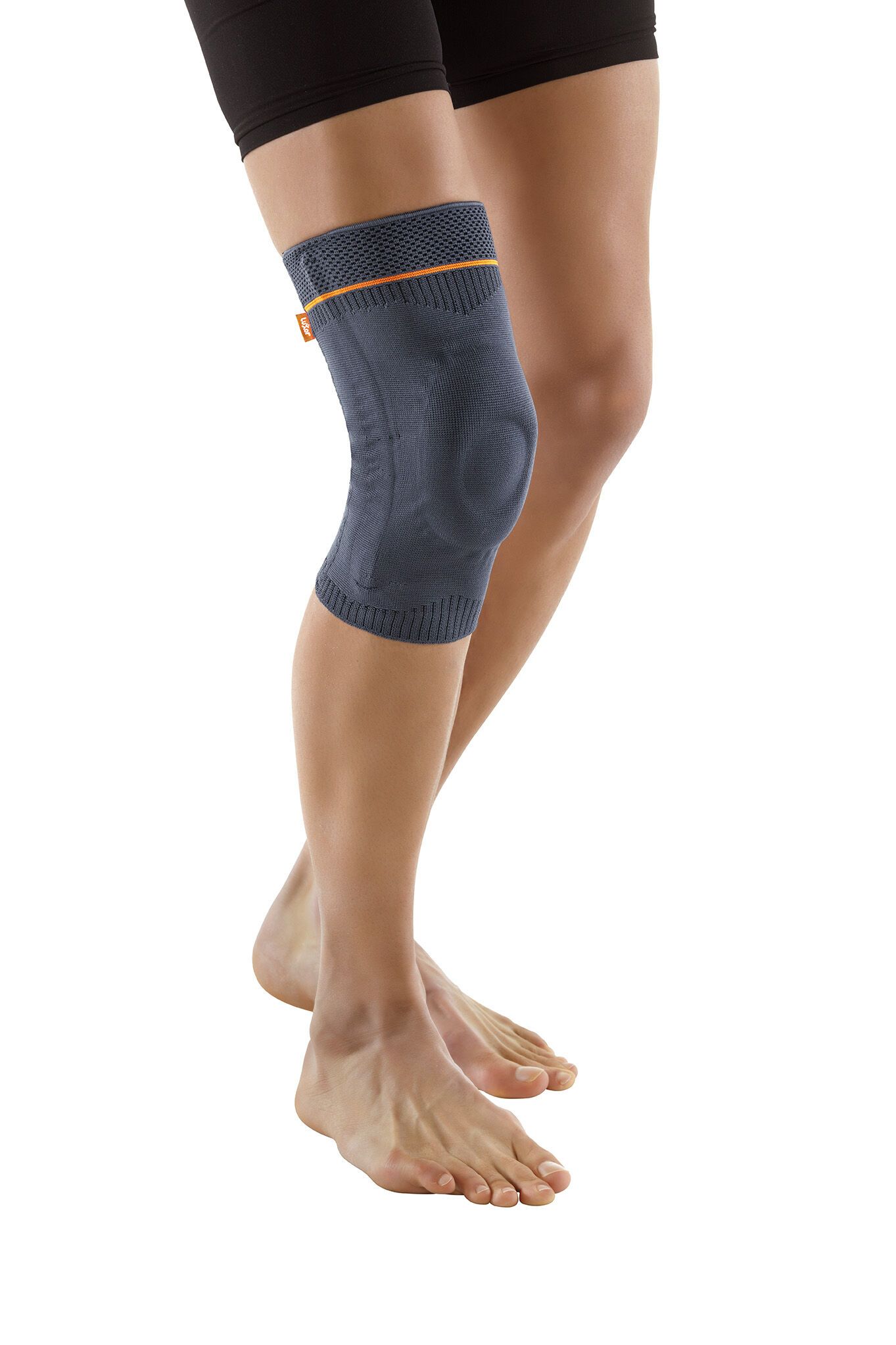 Dunkelgraue Kniebandage am Bein einer Person. Orangefarbener Akzent am oberen Rand. Person steht.