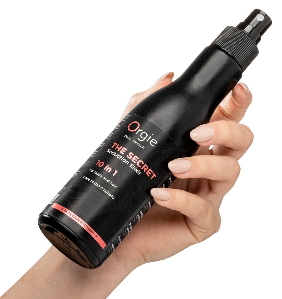 Schwarze Flasche, gehalten in einer Hand. Produktname: Orgie - The Secret Seduction Elixir. Text: 10 in 1, für Körper und Haar.