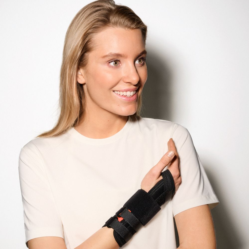 Frau trägt eine schwarze Handgelenkbandage mit Klettverschlüssen am linken Handgelenk.