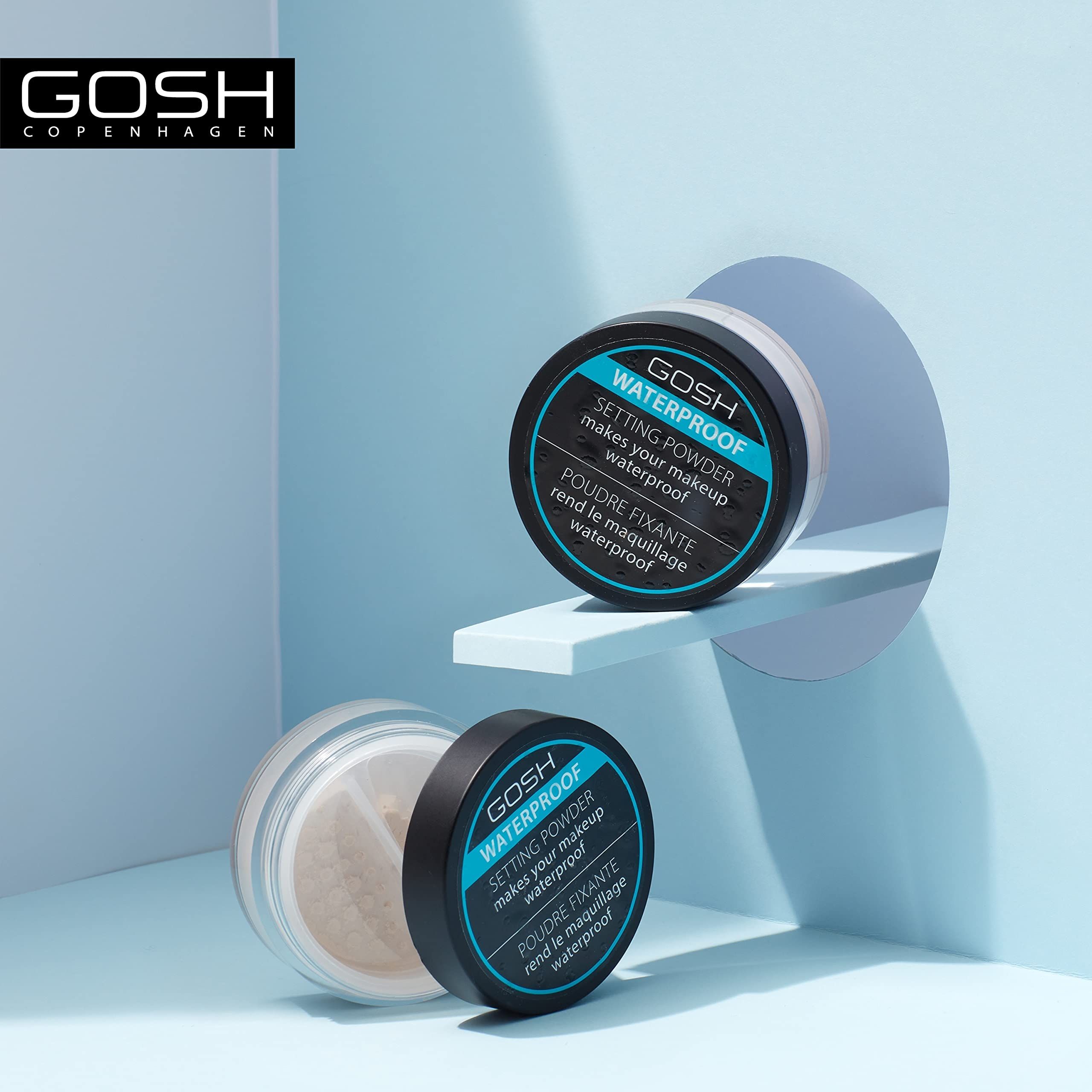 Zwei GOSH WATERPROOF SETTING POWDER Behälter. Einmal geöffnet. Auf blauem Hintergrund. Aufschrift auf den Deckeln.