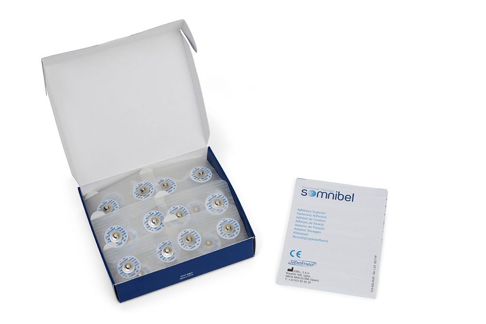 Klebepads in Schachtel, daneben Broschüre. Pads in Folie verpackt. CE-Kennzeichnung und Markenlogo sichtbar.