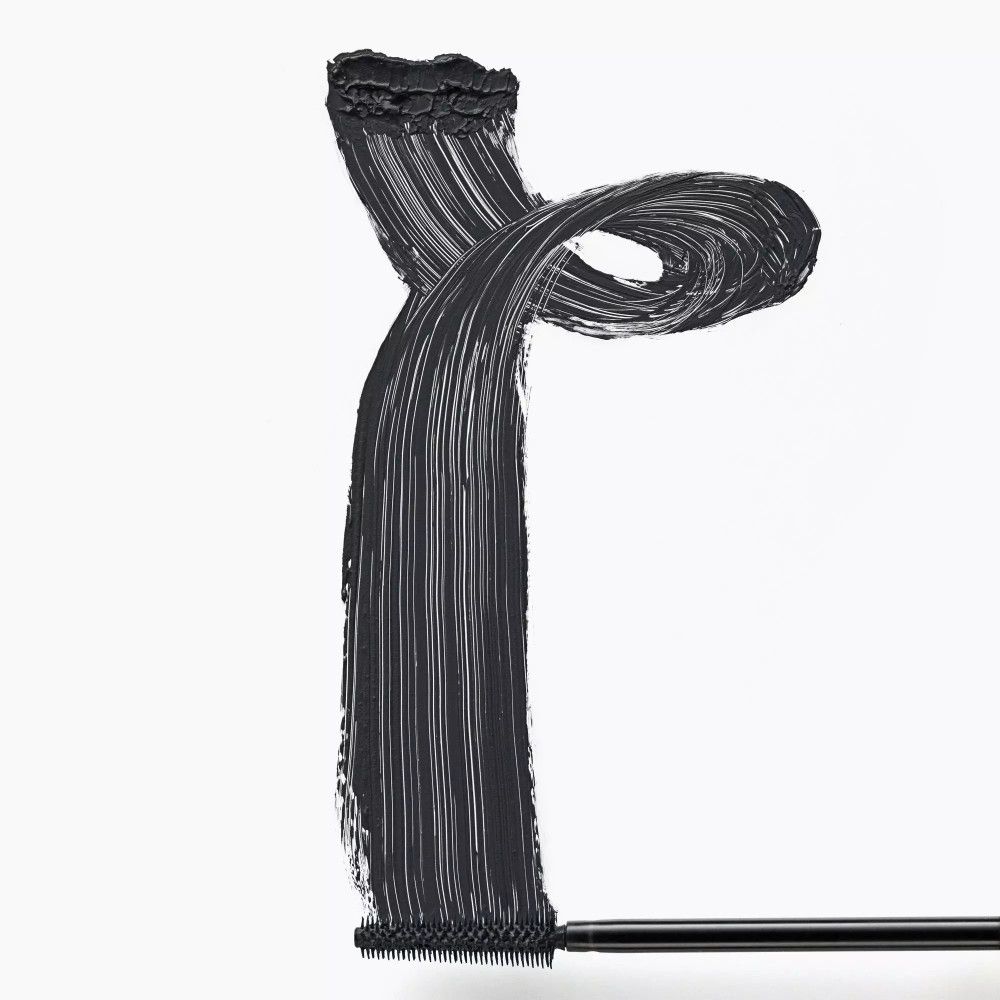 Schwarze Mascara-Textur auf weißem Hintergrund. Die Bürste ist am unteren Ende sichtbar.