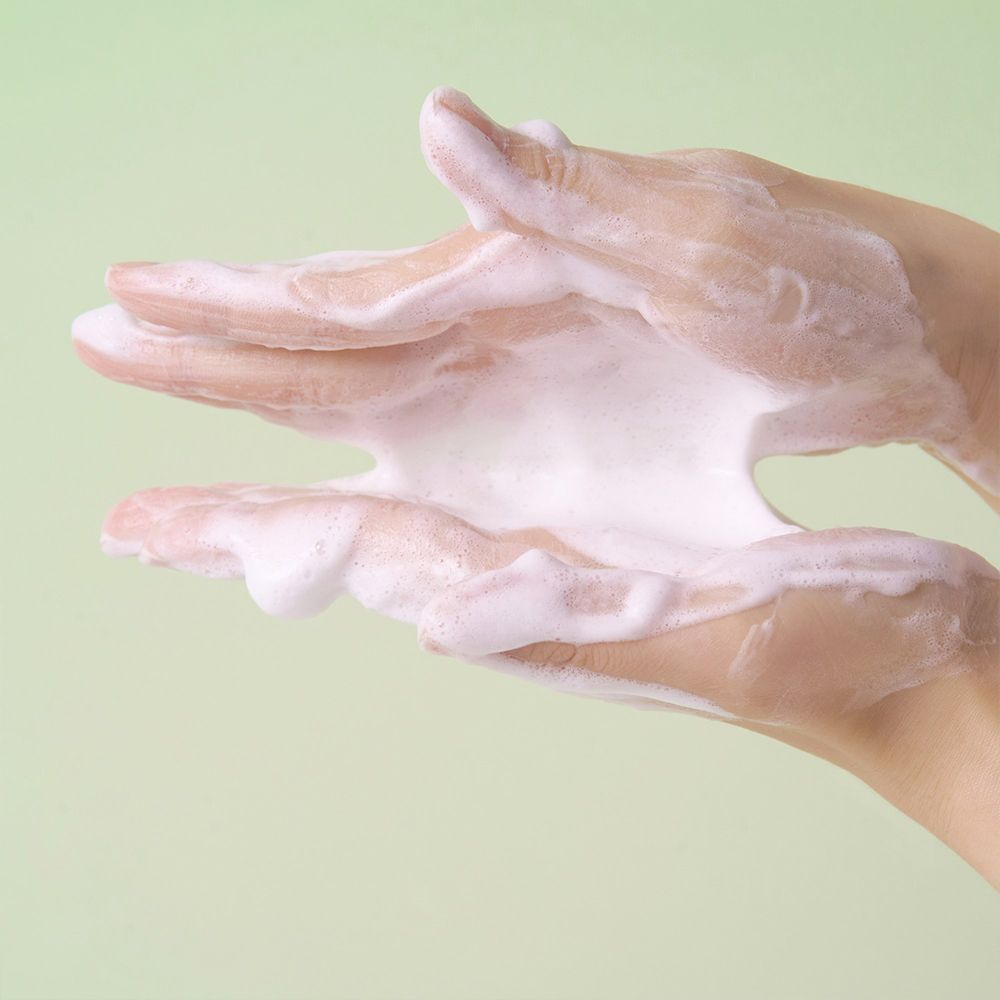 Hände mit schaumigem Reinigungsprodukt, das zwischen den Fingern herausquillt.