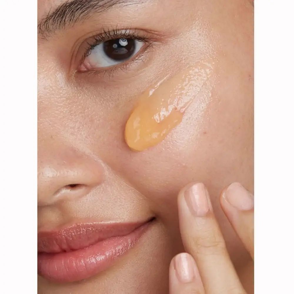 Nahaufnahme eines Gesichts mit aufgetragener, gelblicher Reinigungslotion. Hautpartie mit Finger berührt.