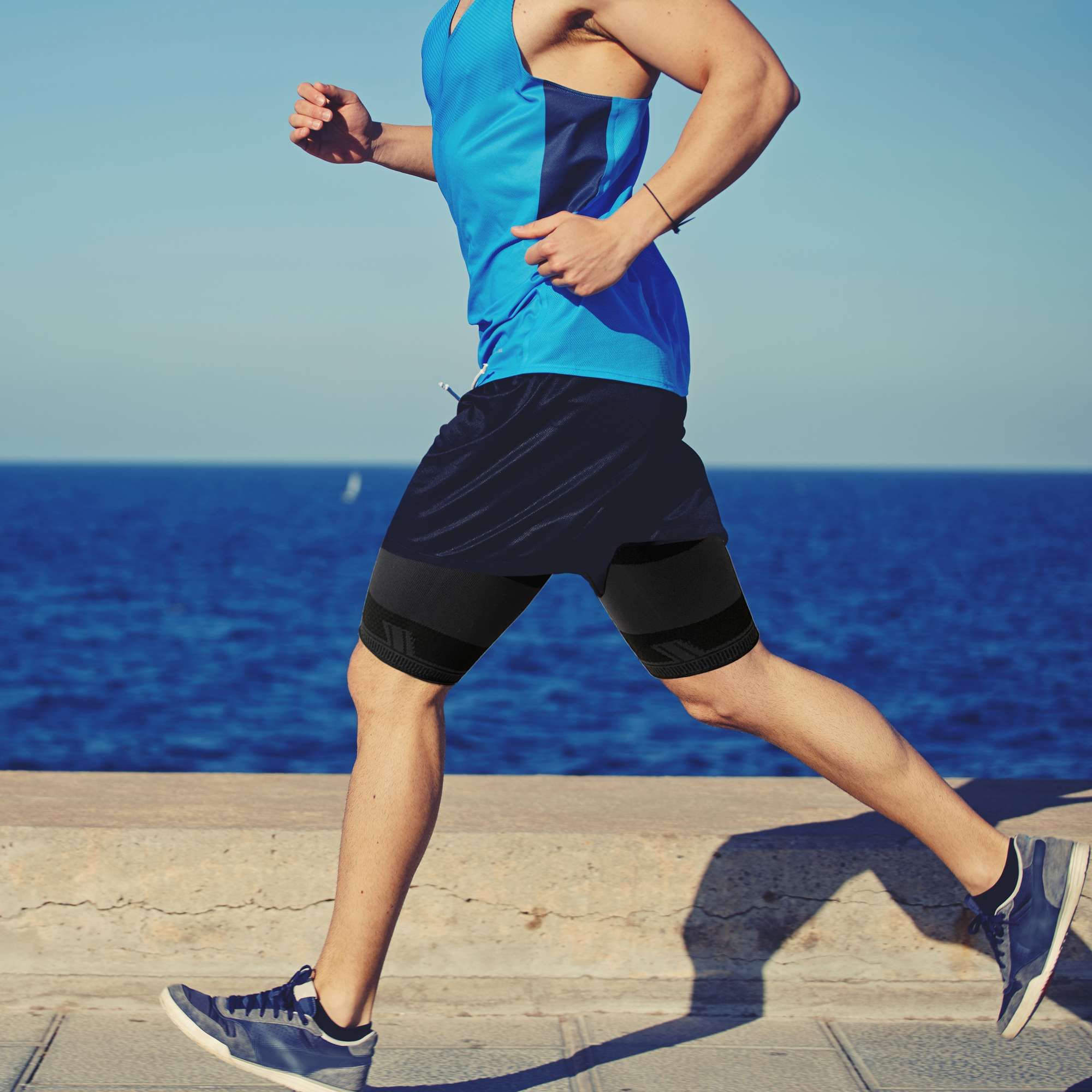Mann beim Laufen am Meer mit Oberschenkelbandage. Schwarze Bandage am Bein.
