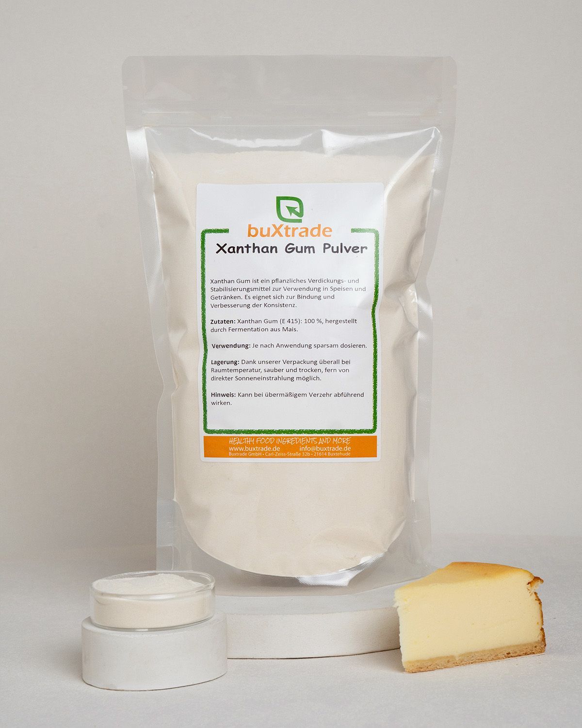Verpackung mit buxtrade Xanthan Gum Pulver neben einem Glasbehälter, einem Holzlöffel und Käsekuchen.