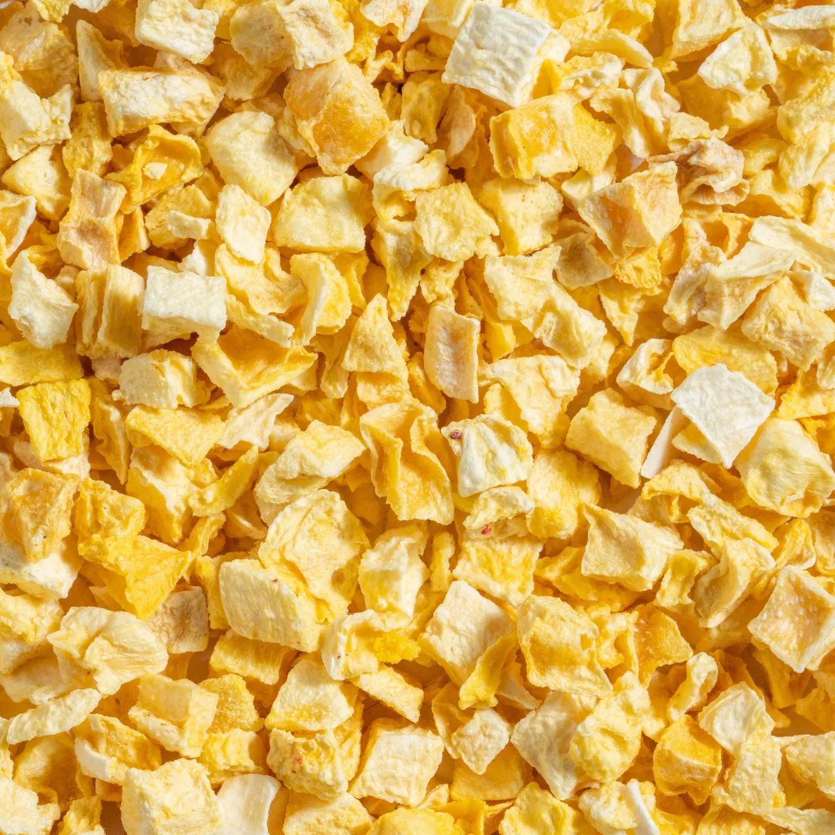 Nahaufnahme von gefriergetrockneten Mango-Stücken. Gelbliche, unregelmäßig geformte Stücke. Textur sichtbar.