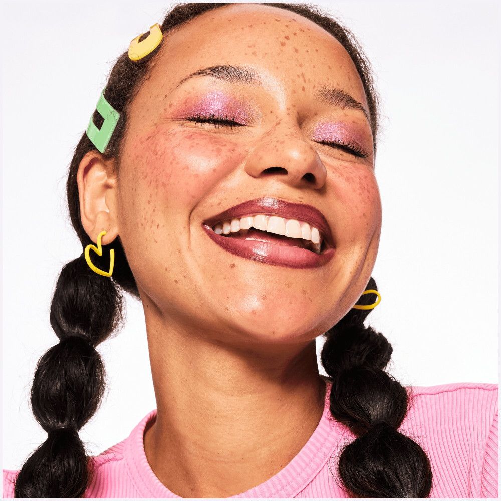 Porträt einer lächelnden Frau mit Lippenstift. Sichtbar sind Lippen, Augen, Haare und Accessoires.