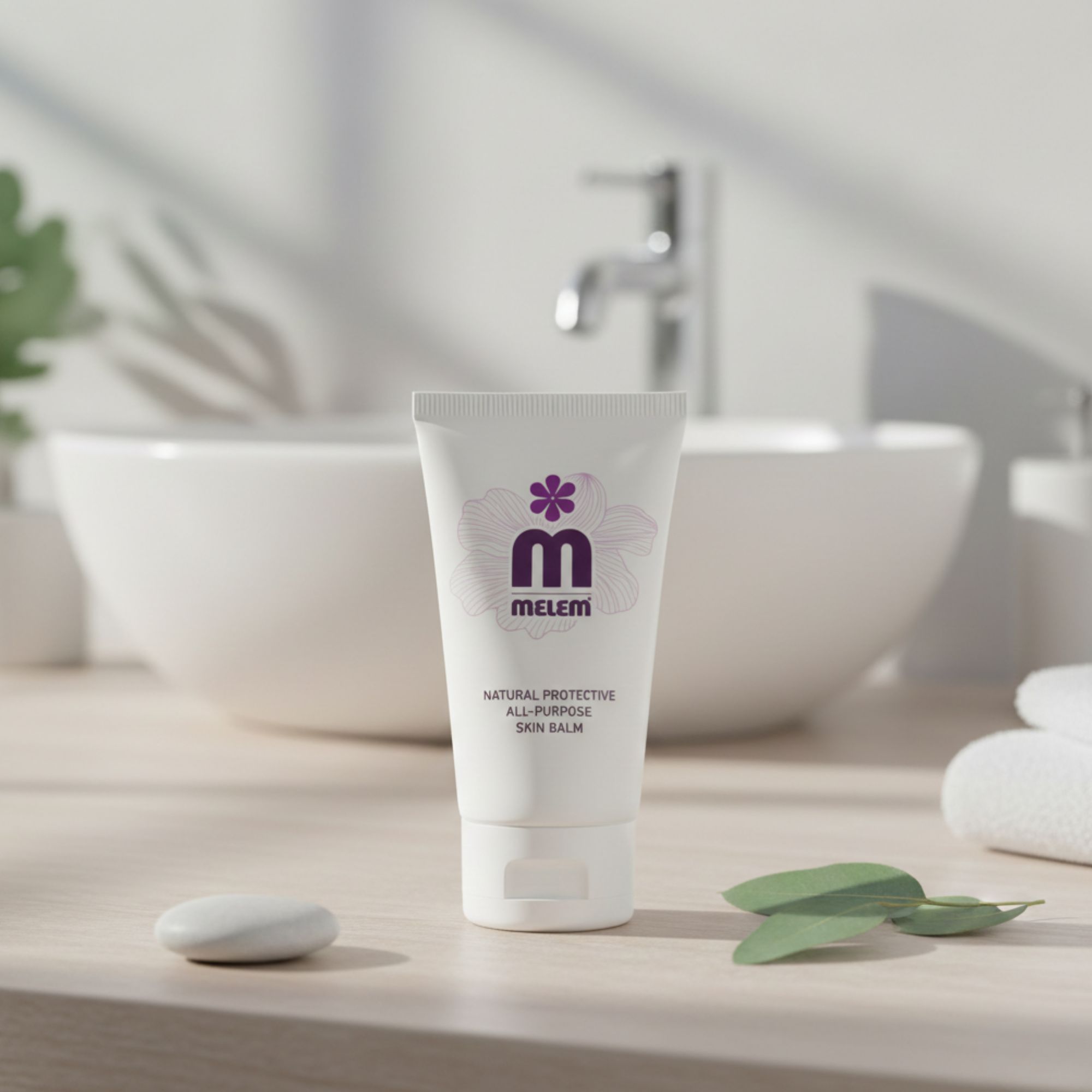Weiße Tube mit lila Logo und Text: Melem, Natural Protective All-Purpose Skin Balm. Vor Waschbecken platziert.