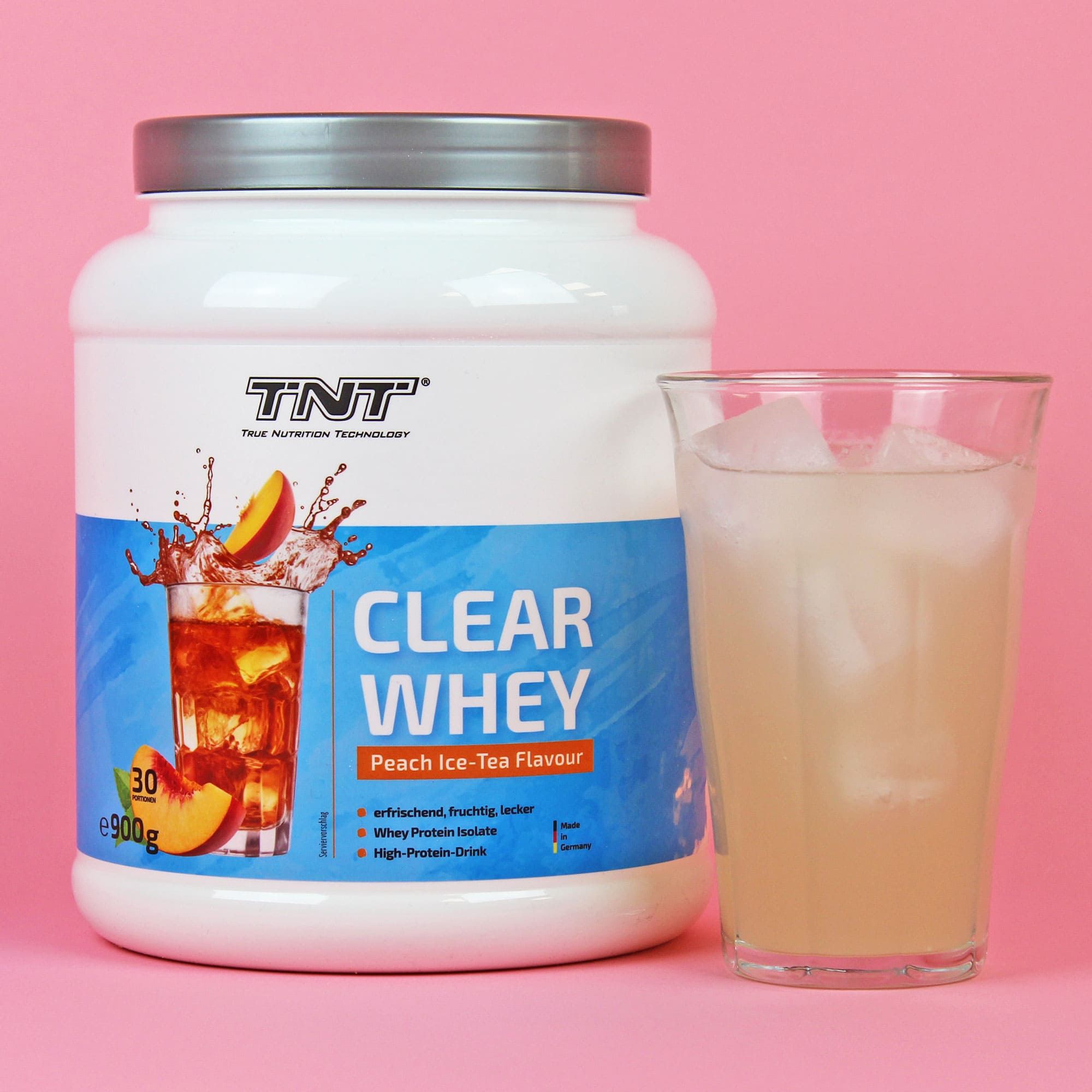 Weiße Dose TNT Clear Whey neben Glas mit Getränk. Aufschrift: Clear Whey, Peach Ice-Tea Flavour. Rosa Hintergrund.