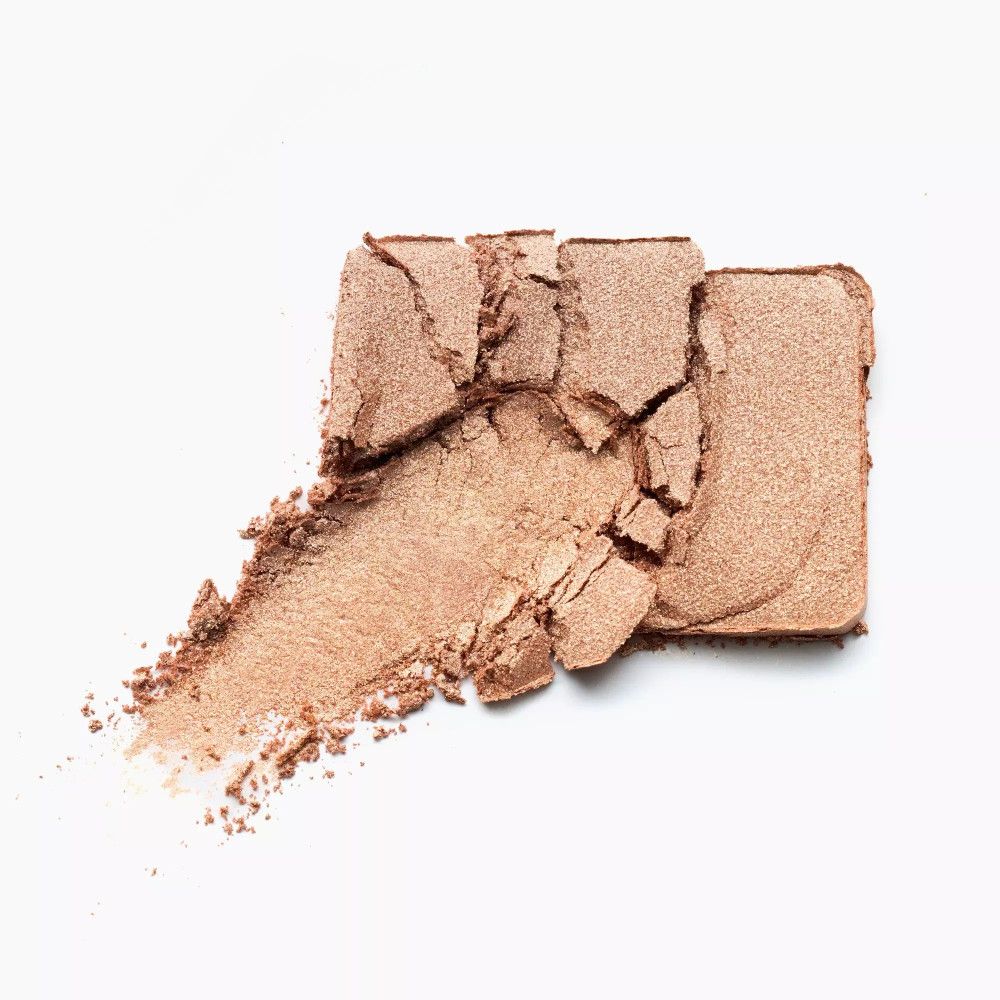 Goldfarbener Lidschatten, zerbrochen in mehreren Teilen, mit einem Pinselstrich auf weißem Hintergrund.