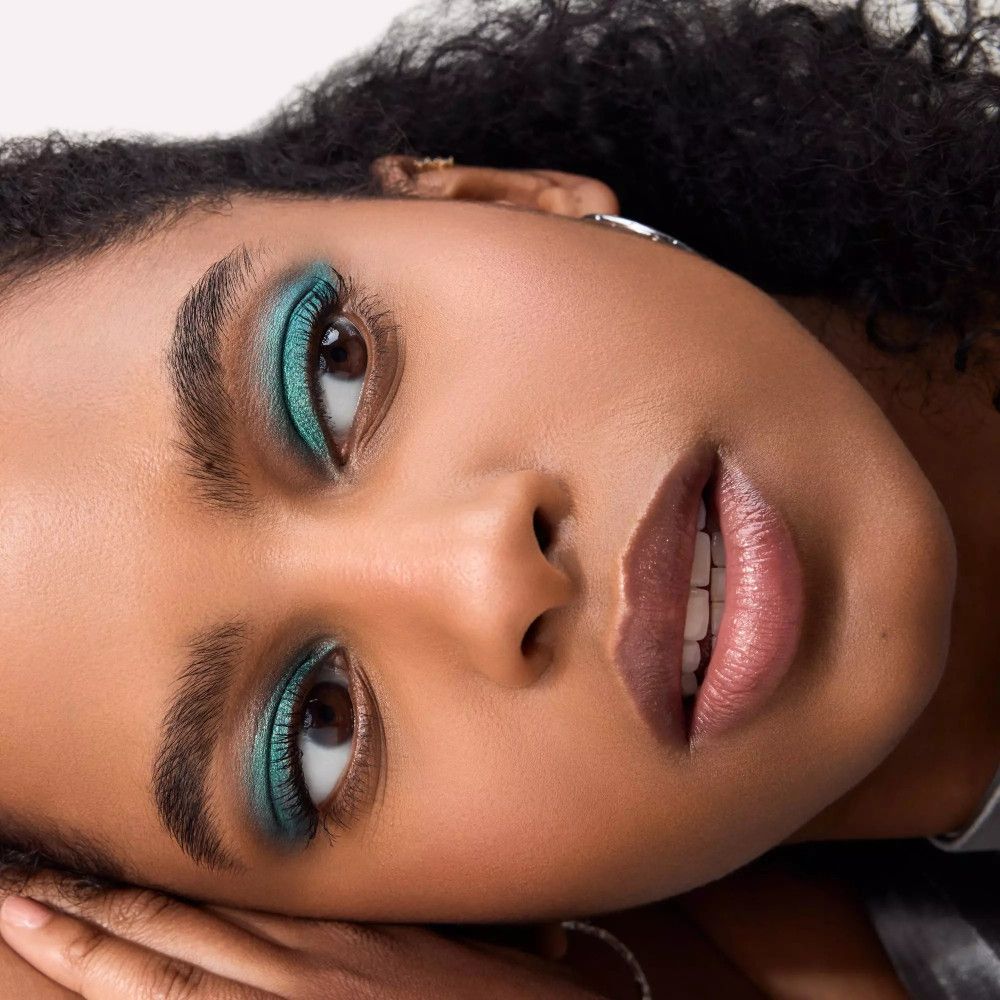 Nahaufnahme eines Gesichts mit grüner Lidschattenfarbe auf den Augenlidern. Die Person liegt.