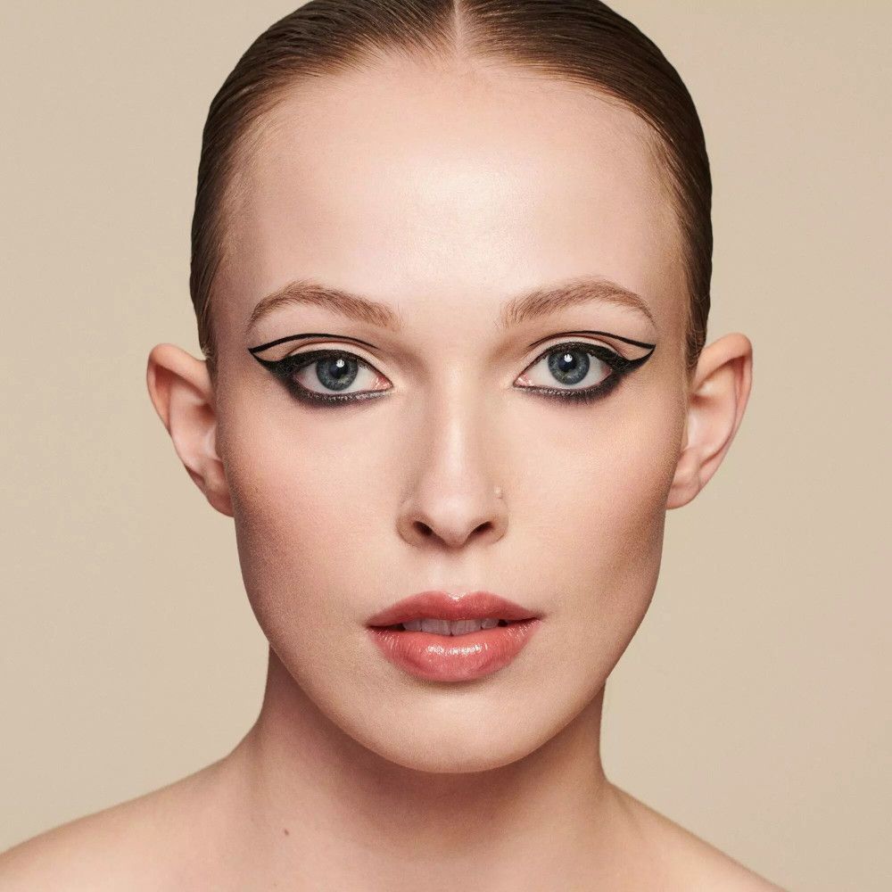 Nahaufnahme eines Gesichts mit Make-up. Schwarzer Eyeliner, rote Lippen. Hintergrund beige.