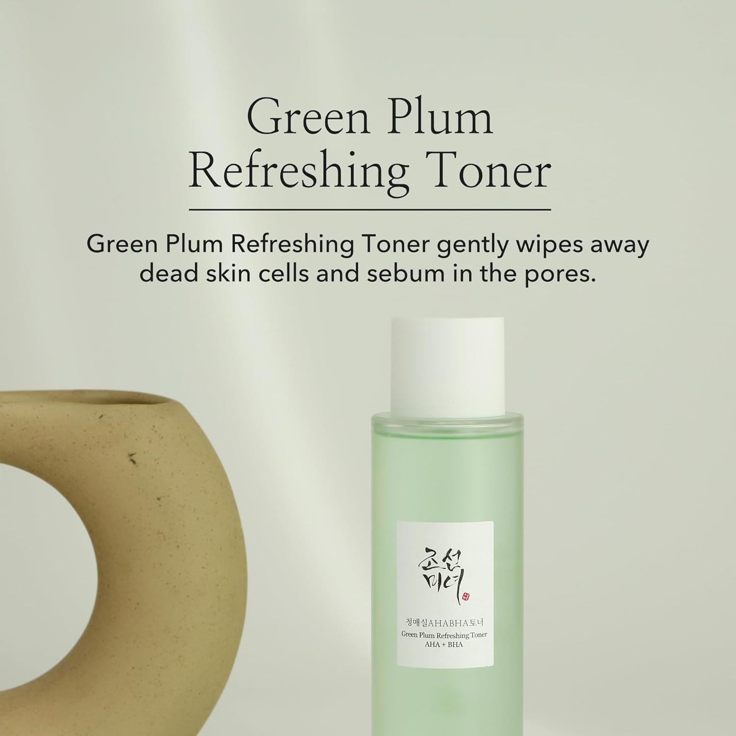Toner-Flasche neben einem dekorativen Objekt. Text: Green Plum Refreshing Toner. Beschreibung: entfernt abgestorbene Hautzellen und Talg.