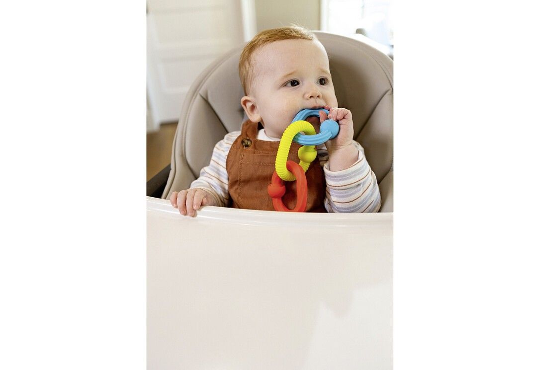 Baby im Hochstuhl beißt auf farbige Silikonringe. Gelb, rot und blau. Ringe mit Noppen und abgerundeten Enden.