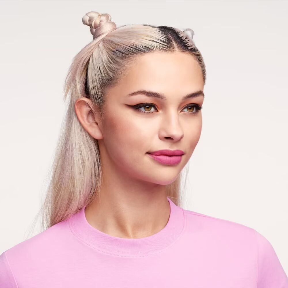 Frau mit rosa Lippenstift. Sie trägt ein pinkfarbenes Oberteil. Blondes Haar, teilweise hochgesteckt.