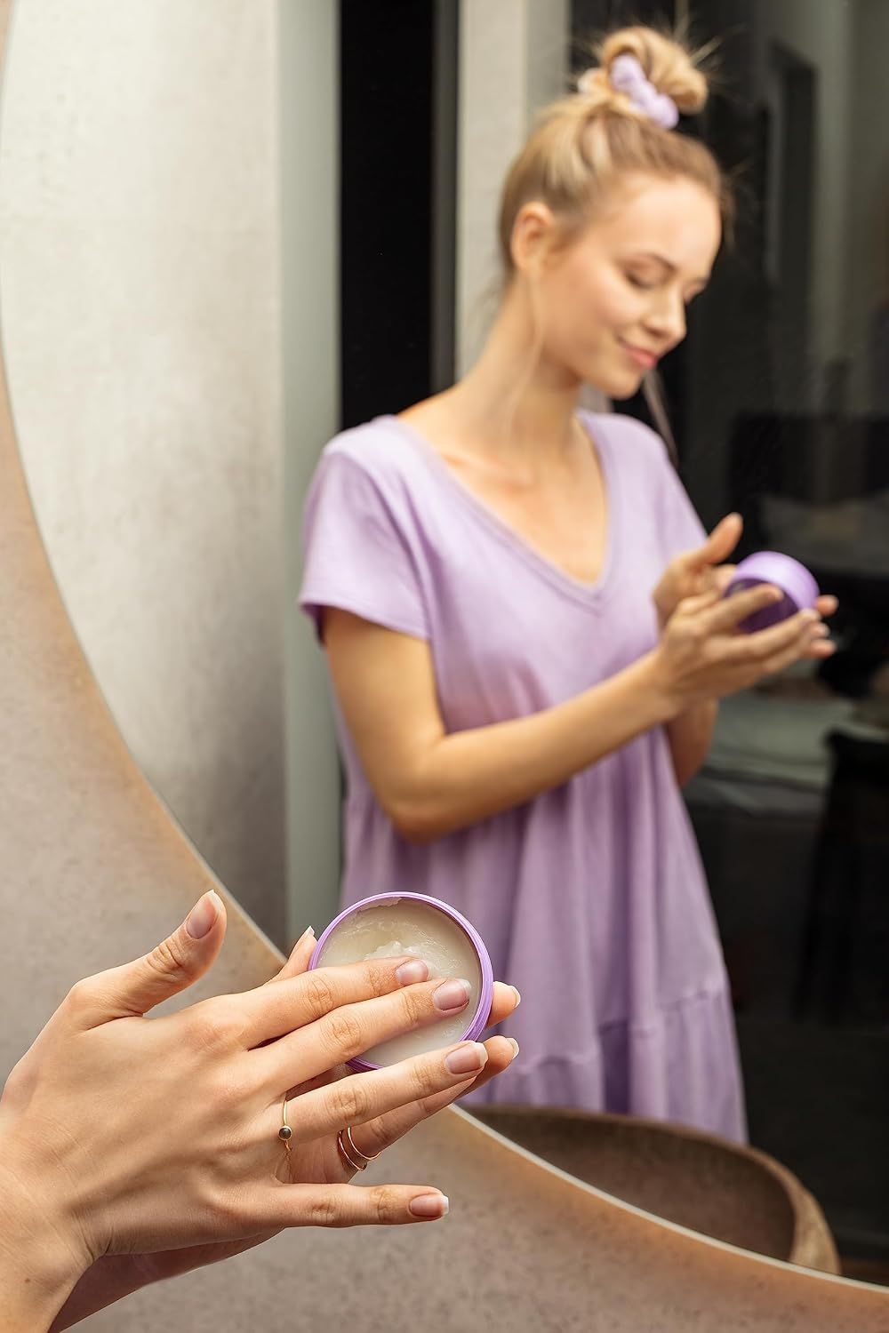 Frau öffnet einen runden, violetten Tiegel mit einer Creme oder Salbe.