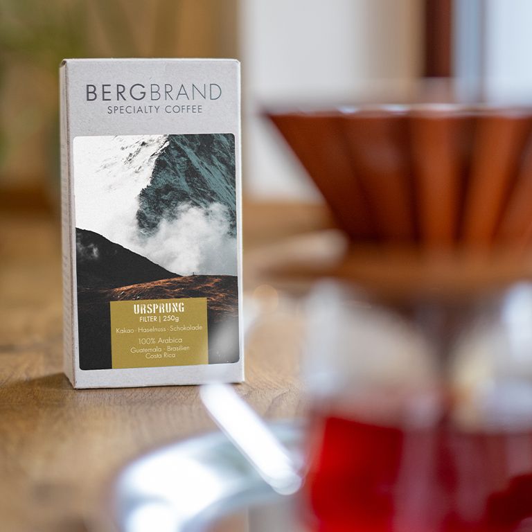 Kaffeepackung mit Bergmotiv. Text: BERGBRAND, Ursprung, Filter, 250g. Zutaten: Kakao, Haselnuss, Schokolade, 100% Arabica.