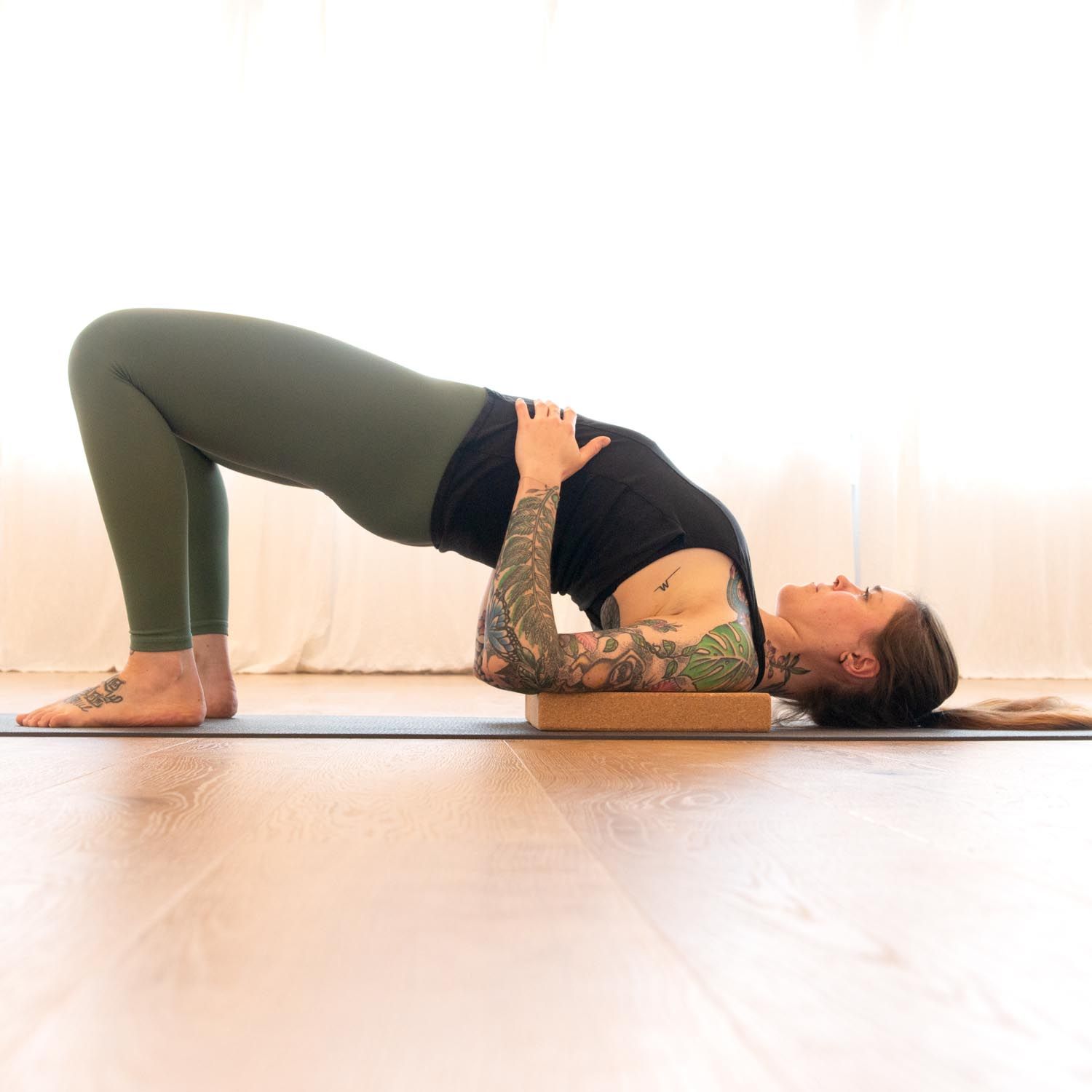 Person in Yoga-Position, Kopf auf einem Block aus Naturkork. Der Block ist hellbraun. Der Hintergrund ist hell.