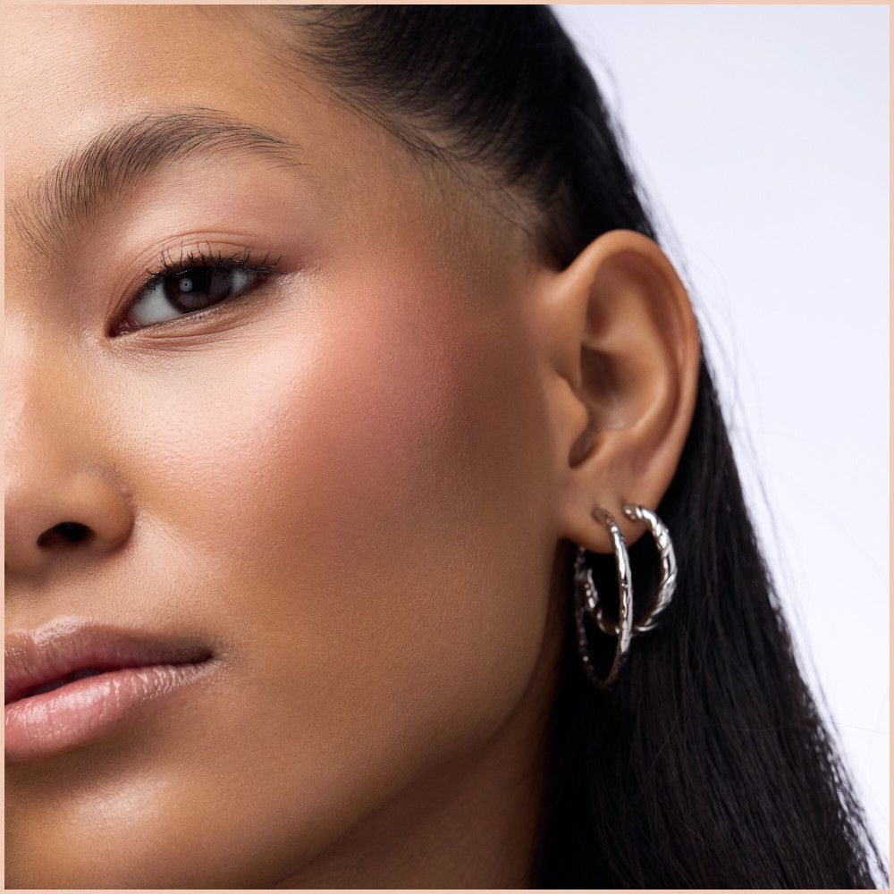 Nahaufnahme eines Gesichts mit rosigem Rouge auf der Wange. Die Frau trägt silberne Creolen.