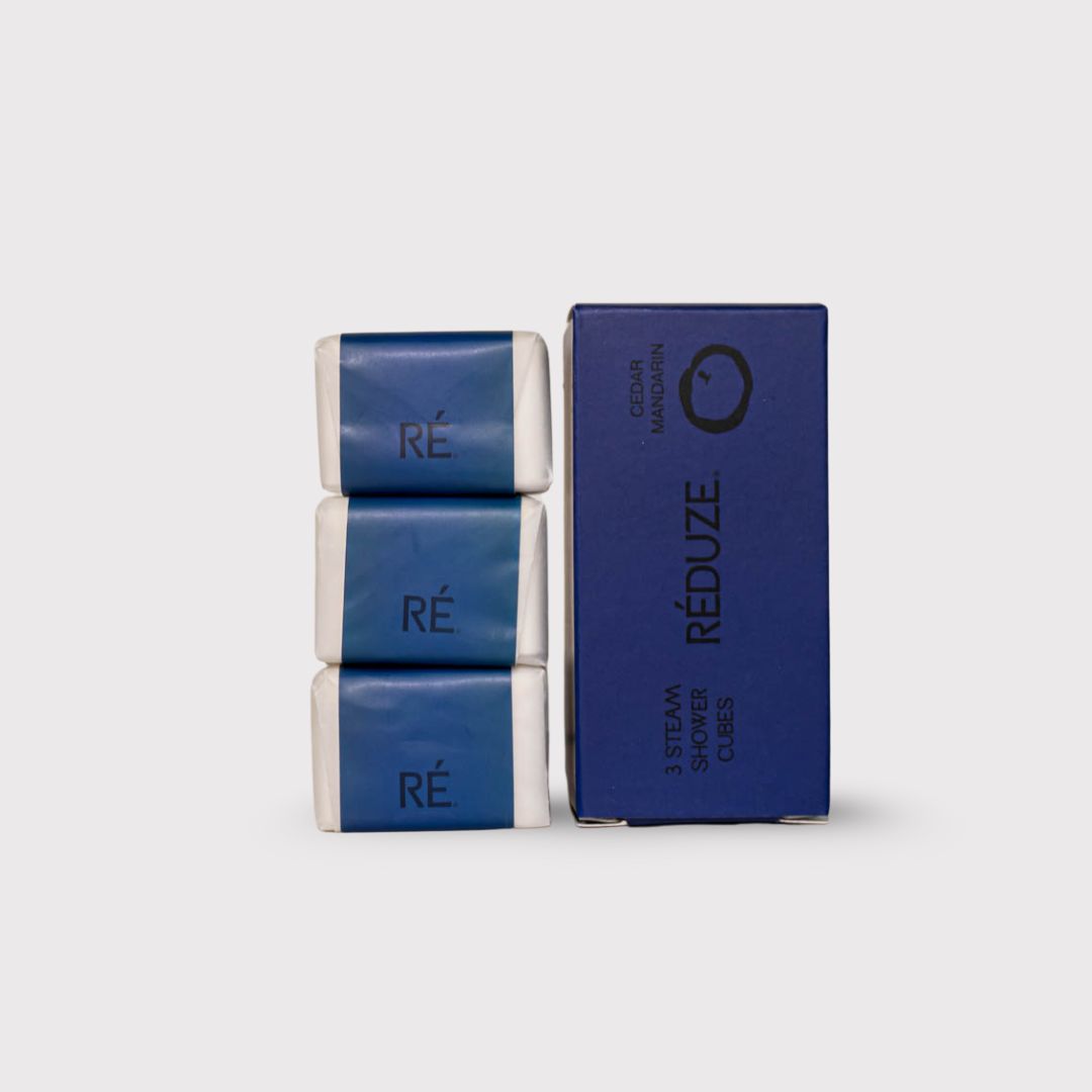 Drei eingepackte Duschwürfel und eine blaue Schachtel. RÉDUZE. Zedernholz & Mandarine. 3 Steam Shower Cubes.