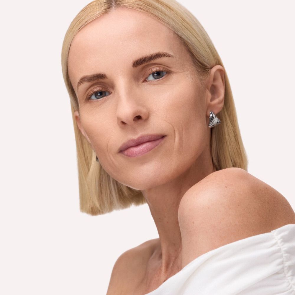 Porträt einer Frau mit blonden Haaren und blauen Augen. Sie trägt Ohrringe.