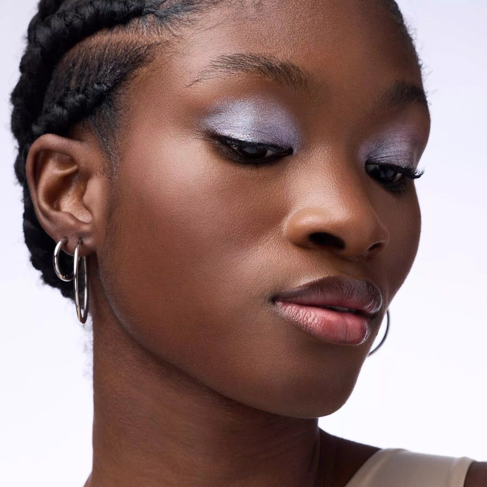 Porträt einer Frau mit silbernem Lidschatten. Eyeliner und Ohrringe. Keine Marke oder Produktname sichtbar.